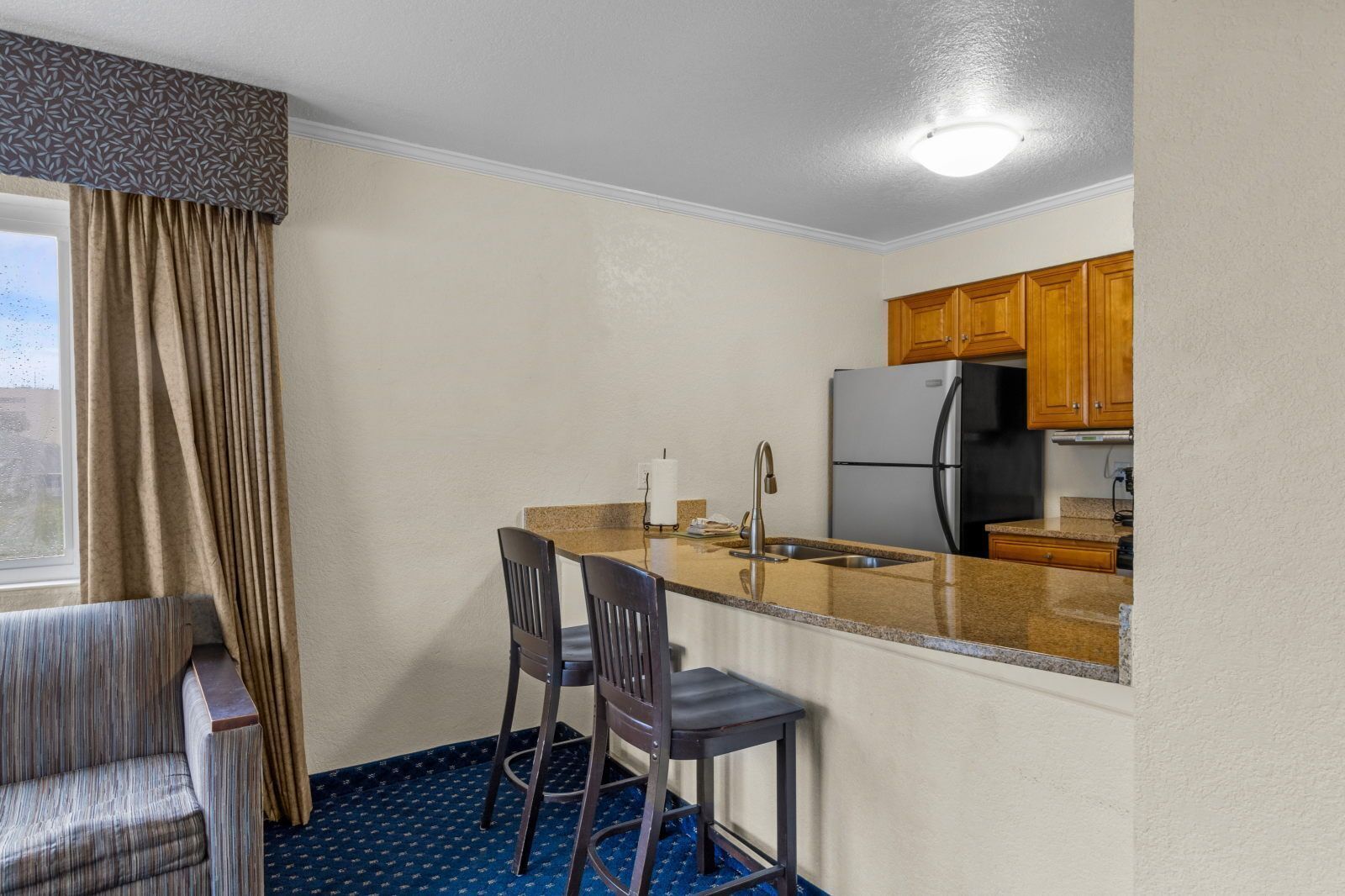 A compact kitchen with a refrigerator, sink, and two bar stools.