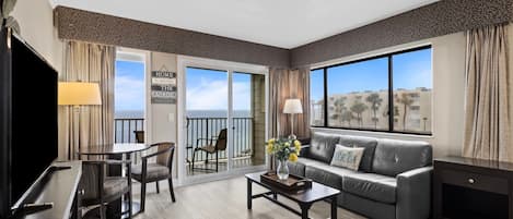 A hotel room with a balcony, a sofa, a coffee table, a TV, and a dining area.