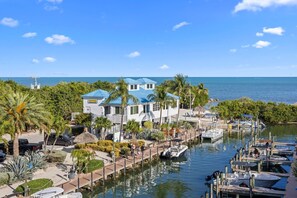 A waterfront property with a dock, a house with a blue roof, and a marina with boats.