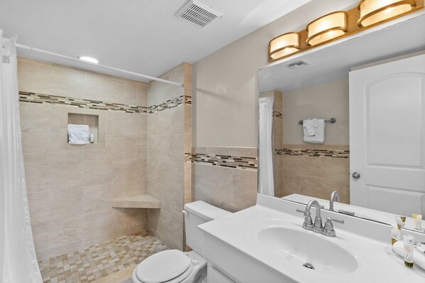 A bathroom with a shower, toilet, sink, and a mirror with lights.
