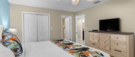 Un dormitorio con una cama, ventilador de techo, televisor y cómoda.