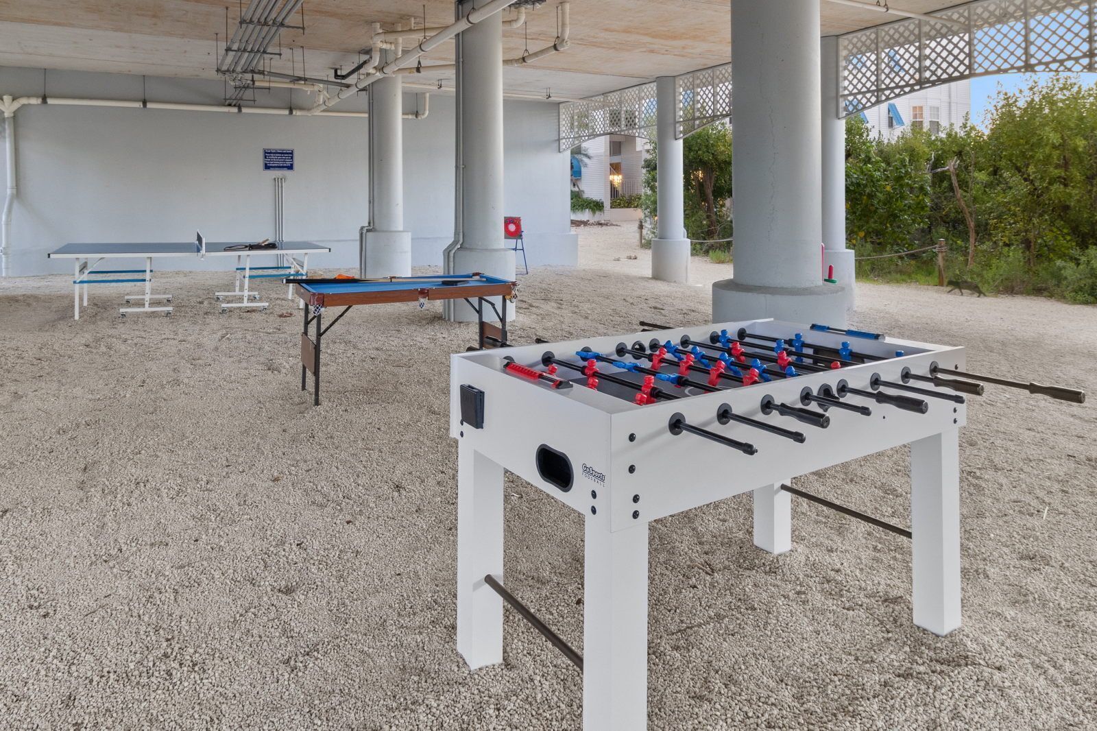 Una mesa de fútbol de mesa, una mesa de ping pong y una mesa de billar en un espacio al aire libre con techo.