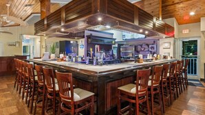 A bar area with a central bar, multiple stools, and a high ceiling with wooden beams.