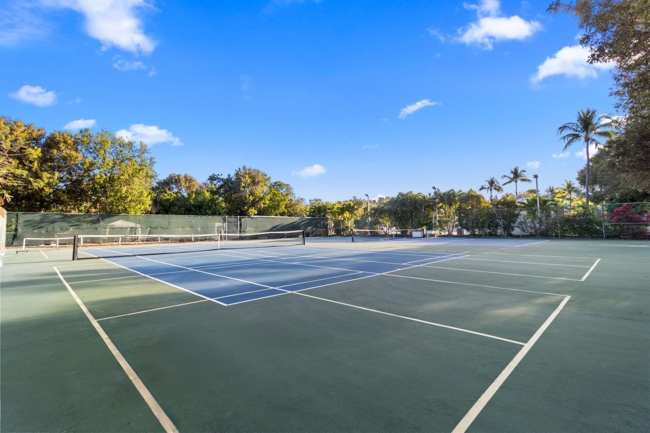 An outdoor tennis court with a net, surrounded by trees and a clear sky.
