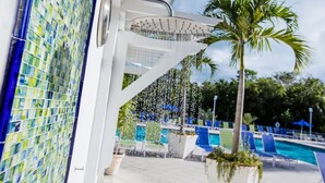 A poolside area with a showerhead, a palm tree, and lounge chairs.