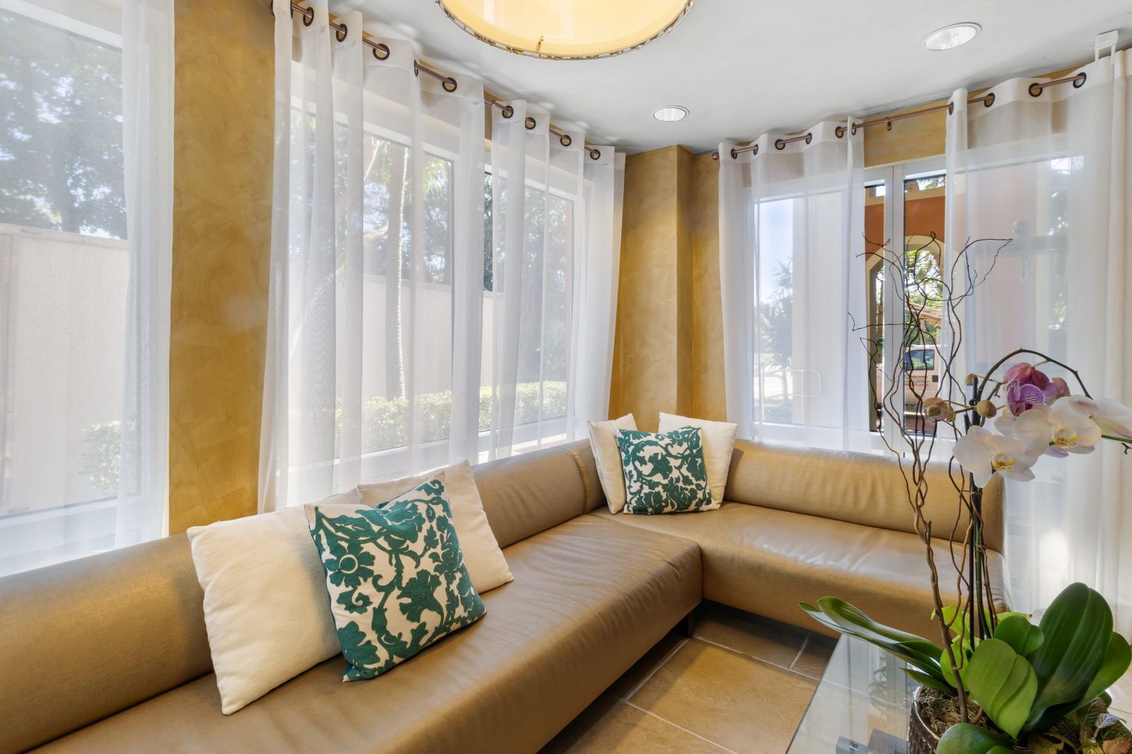 Un salón moderno con un sofá seccional color beige, cortinas de gasa y una orquídea en maceta.