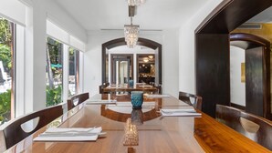 A dining area with a long wooden table, chairs, a chandelier, and large windows.