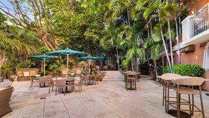 An outdoor patio area with wicker furniture, green umbrellas, and a stone-tiled floor.