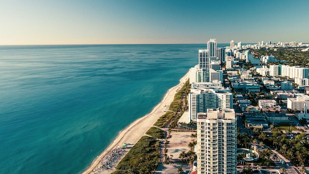 Paisagem costeira urbana com edifícios altos, uma praia e céu claro.