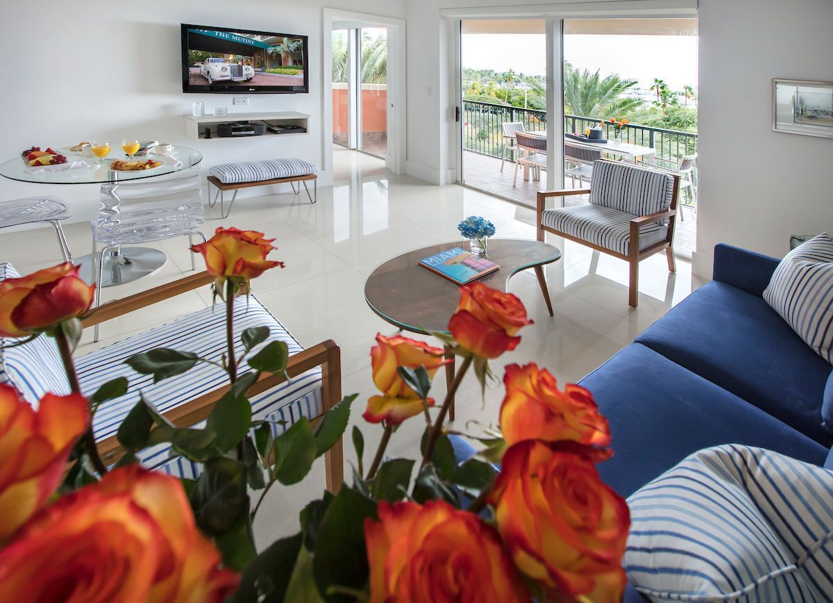 A modern living room with a blue sofa, striped chairs, a glass coffee table, and a TV mounted on the wall.