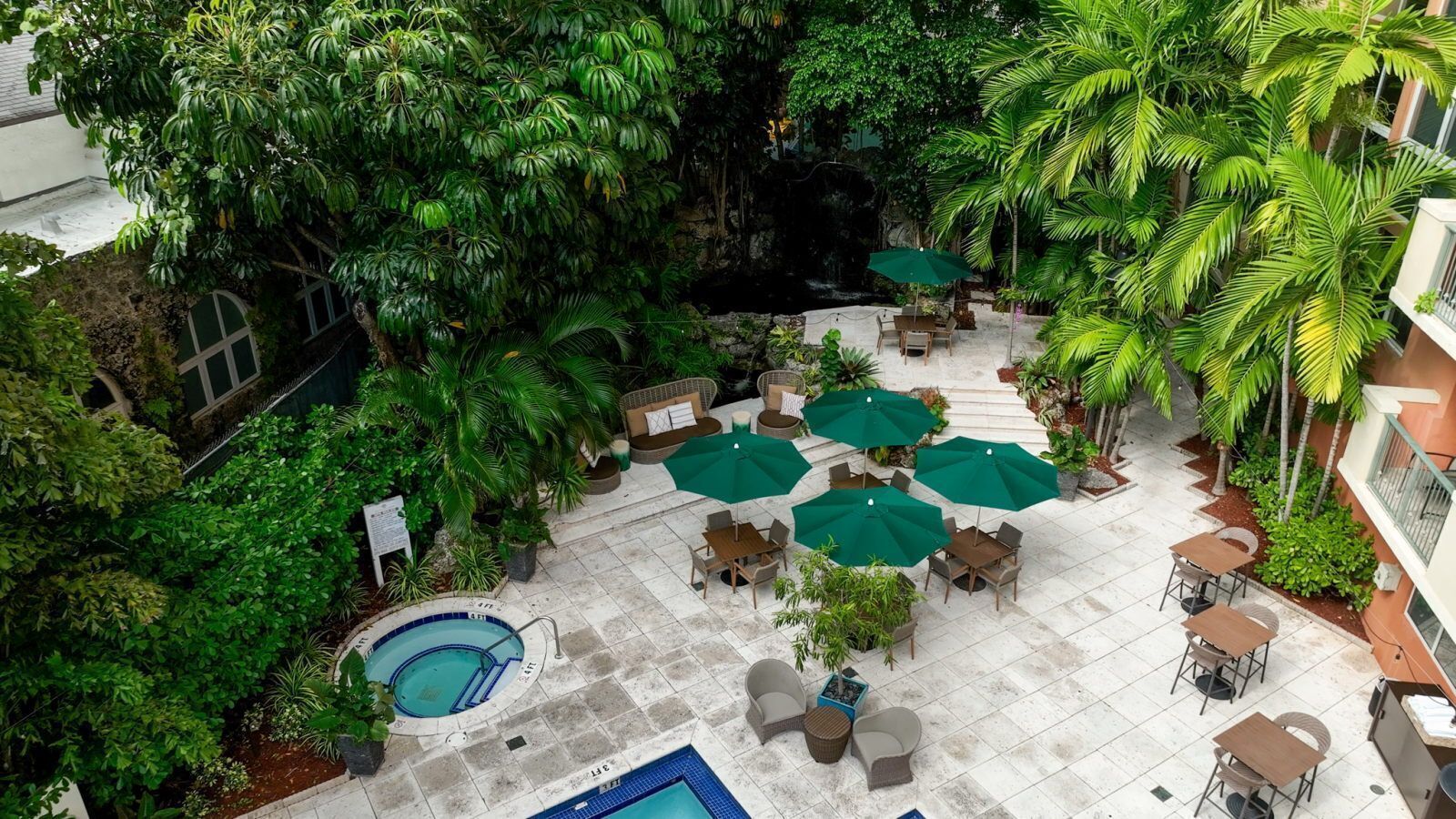 Un espace extérieur avec piscine, agrémenté de plusieurs coins salon et de parasols, le tout entouré d’une végétation luxuriante et d’arbres.
