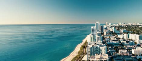 A coastal cityscape with high-rise buildings, a beach, and a clear sky.