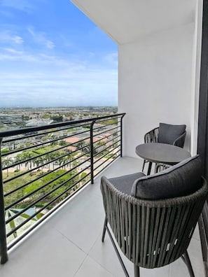 A balcony with a view of a cityscape, a table, and two chairs. - Upscale 2BR City-View Suite | Pool, Sauna & Spa (Miami)