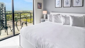 A modern bedroom with a large bed, a nightstand, a lamp, and framed botanical prints on the wall. - Luxury Studio Suite w/ Golf View | Sauna + Pool (Miami)
