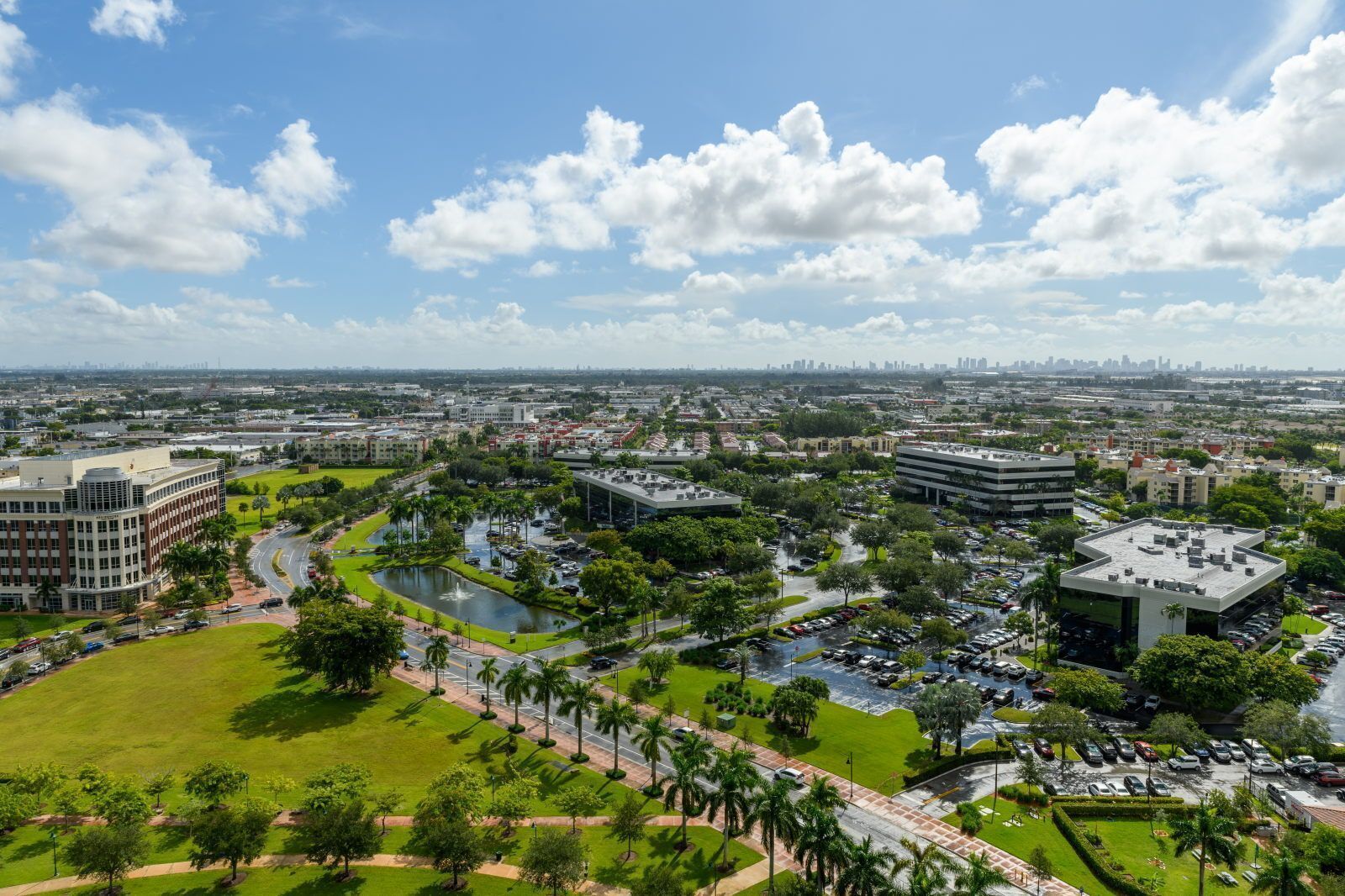 Un paisaje urbano con un complejo de edificios, un parque central con un estanque y un área de estacionamiento.