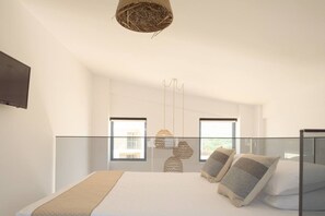 A modern bedroom with a large bed, two windows, a TV, and hanging lights. - New Villa W/Heated Pool, 5 min Walk to Beach & Amenities (Georgioupoli)