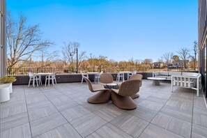 Um terraço no telhado com móveis de exterior, vista para árvores e um edifício ao fundo.