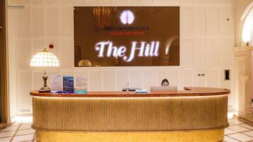 Een receptiebalie met een flatscreen-tv waarop het bord 'The Hill' staat, een lamp en informatiefolders.