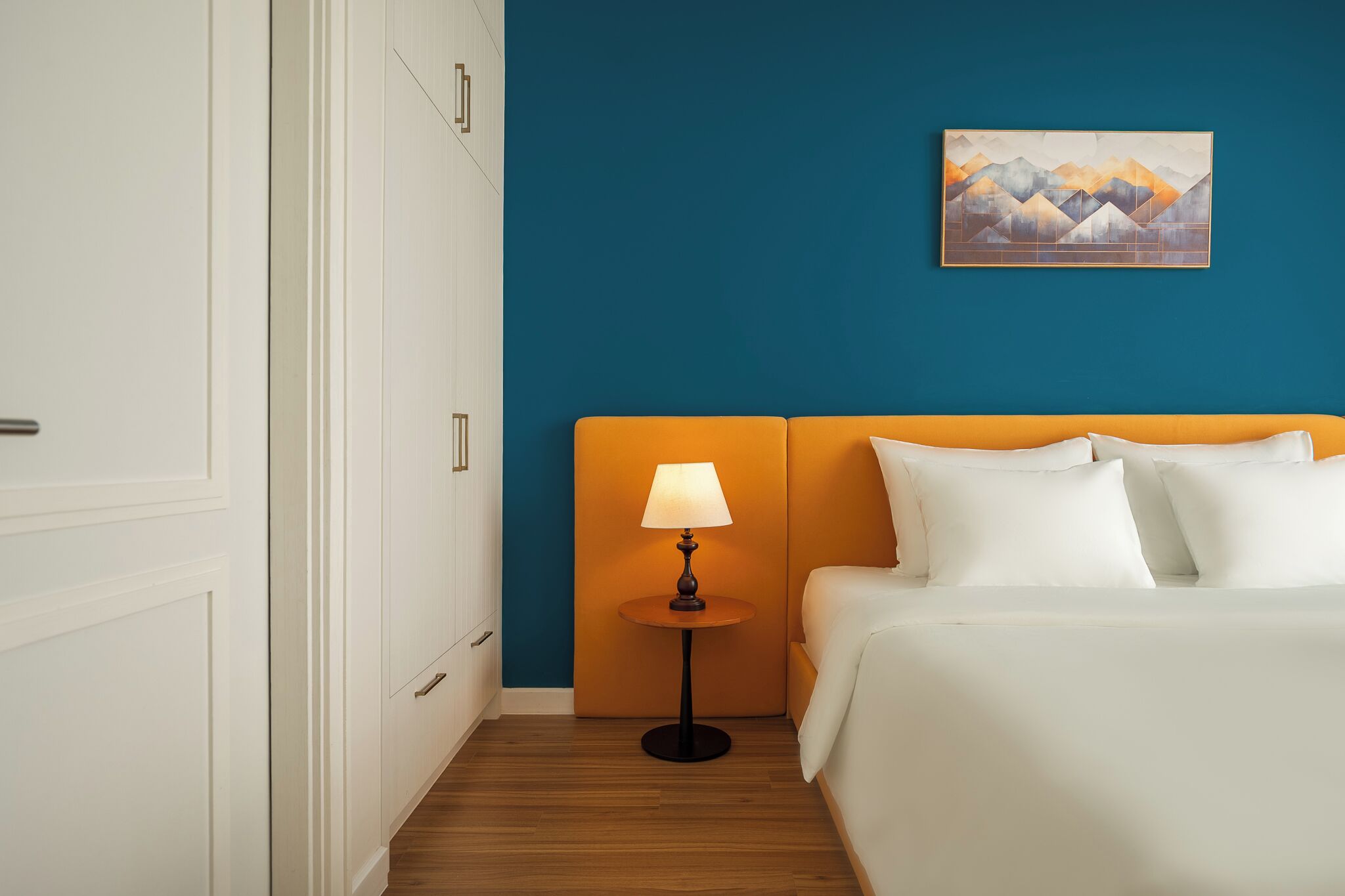 Ein Hotelzimmer mit Bett, Nachttisch mit Lampe, einem Bild an der Wand und einem Schrank.
