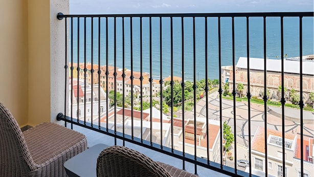 Un balcón con mobiliario de mimbre y vista al mar y edificios.
