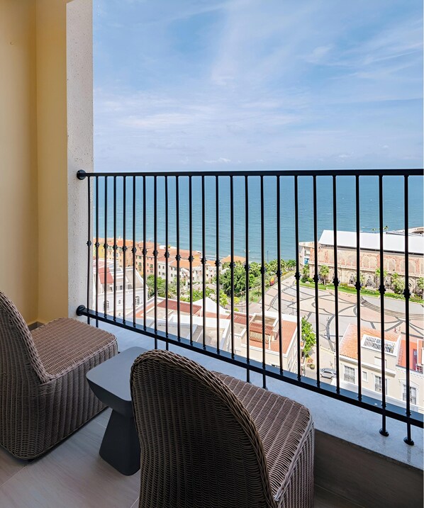 A balcony with wicker furniture and a view of the sea and buildings. - JM Apartment Hillside Phu Quoc (An Thoi)