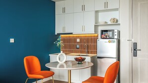Una cocina moderna con armarios blancos, un refrigerador blanco y una mesa redonda con dos sillas naranjas.