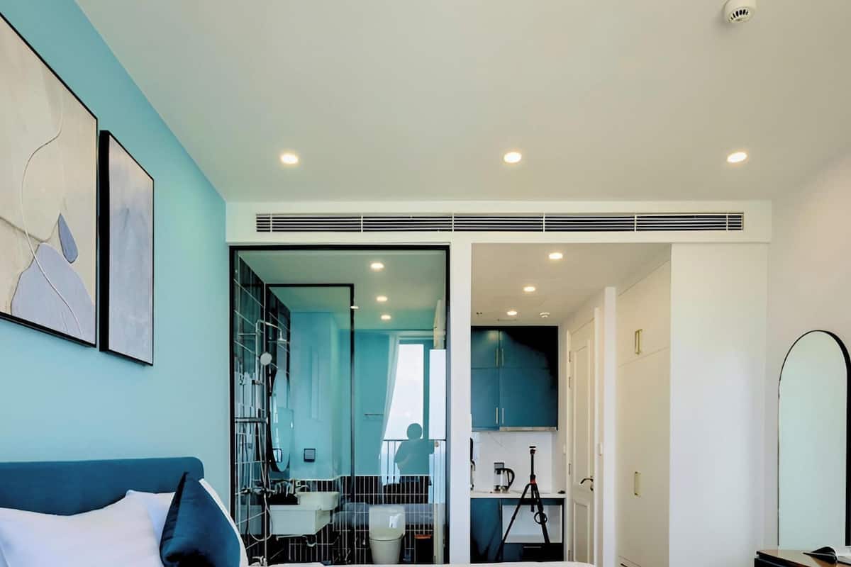 A modern hotel room with a large bed, a bathroom with a glass partition, and a kitchenette.