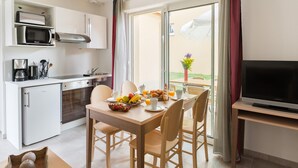 A compact kitchen with a microwave, coffee maker, and a small refrigerator. There is a dining area with a table set for two, featuring a fruit bowl, croissants, and a glass of orange juice. A television is placed on a stand to the right. - Perigord Retreat Near Lascaux (Montignac)