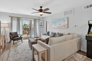 A living room with a sofa, a coffee table, a chair, a ceiling fan, and a painting on the wall. - La Mirage 108: Spacious 3BR condo in Port Aransas with resort access. (Port Aransas)
