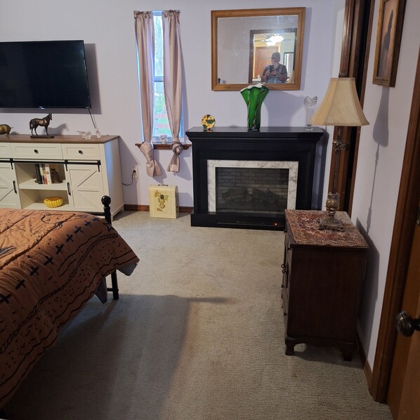A bedroom with a bed, a dresser, a television, a fireplace, and a mirror.