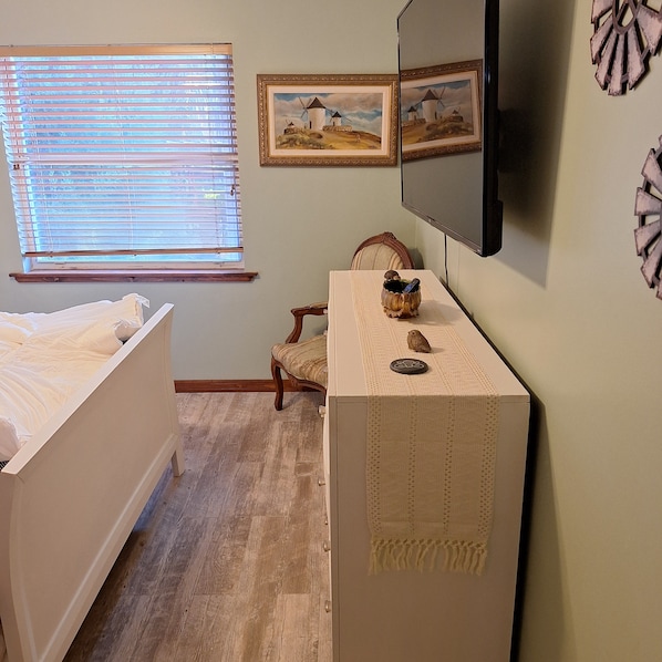 Un dormitorio con una cama, una silla, un televisor y dos cuadros en la pared.