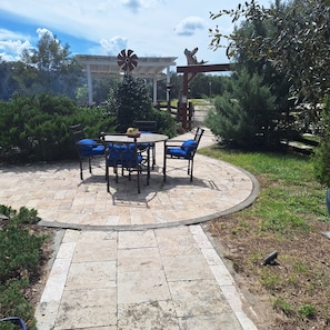 Un patio al aire libre con una mesa redonda y sillas, rodeado por un camino de piedra.