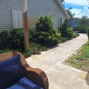 A pathway leading to a house with a wooden post and a wicker chair with a cushion.
