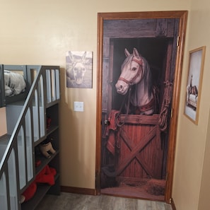 A room with a door that has a horse head design, a wooden door frame, and a small shelf with a picture of a horse.