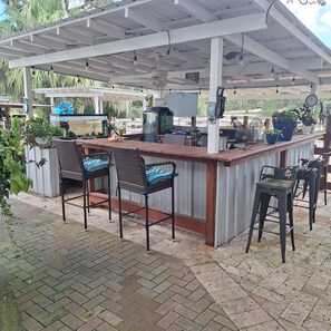 An outdoor bar area with a wooden counter, wicker bar stools, and a ceiling fan.
