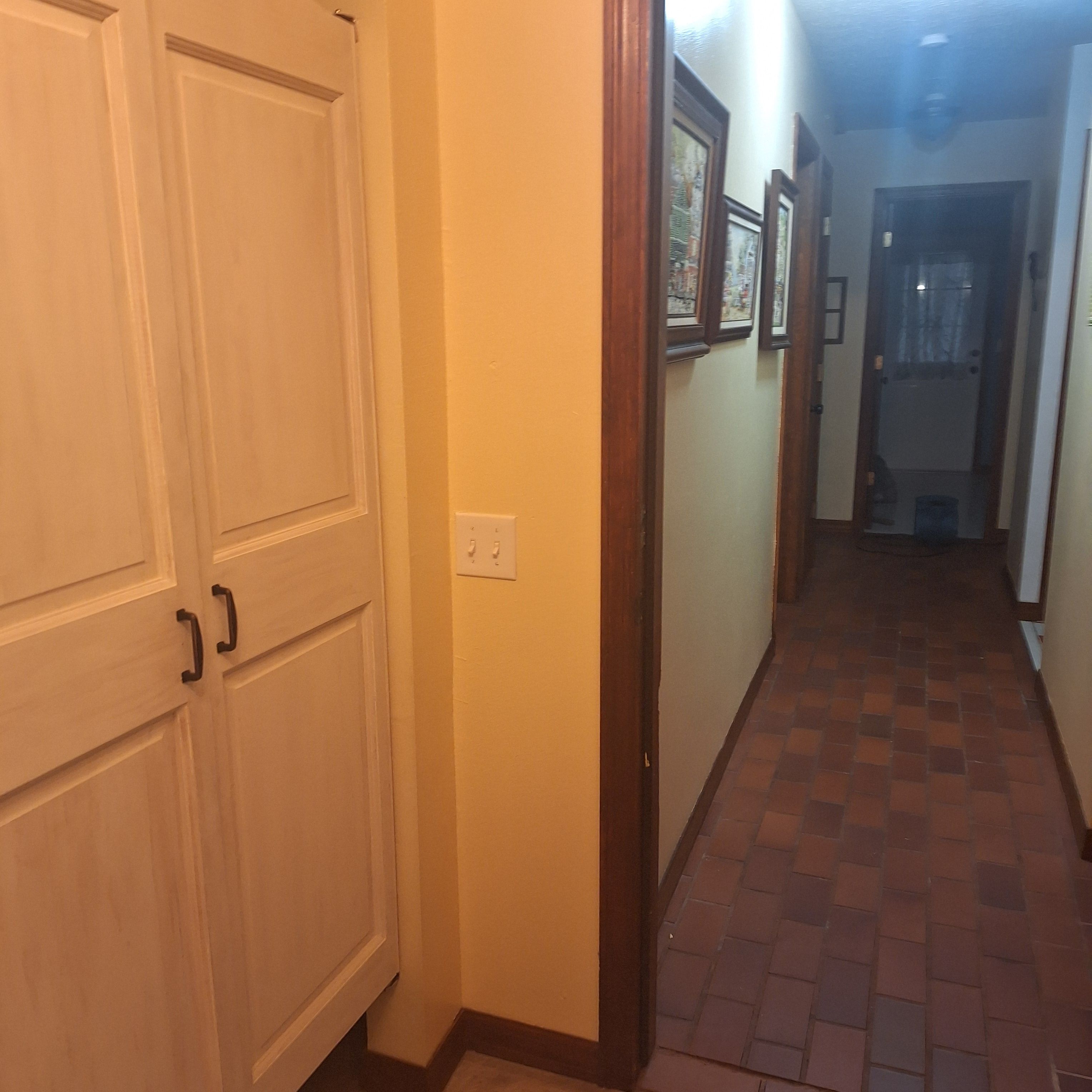 A hallway with a tiled floor, a white door with a handle, and a light switch on the wall.