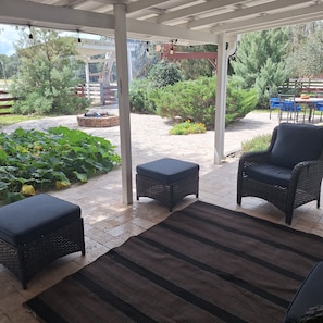 A covered patio area with outdoor furniture, a fire pit, and a view of the surrounding garden and trees.