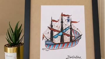 Una obra de arte enmarco que muestra un barco con el año 1759, una pequeña planta en maceta y un recipiente dorado con texto.
