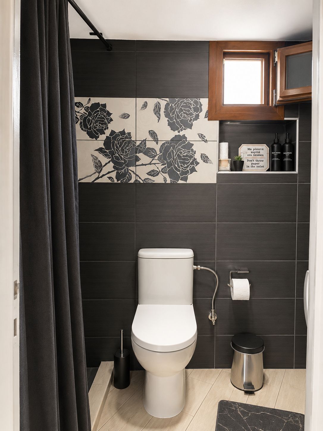 A modern bathroom with a toilet, a trash bin, a toilet brush, a shower curtain, and a cabinet with toiletries.