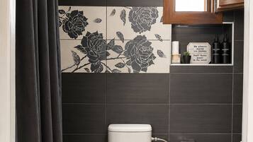 A modern bathroom with a toilet, a trash bin, a toilet brush, a shower curtain, and a cabinet with toiletries.