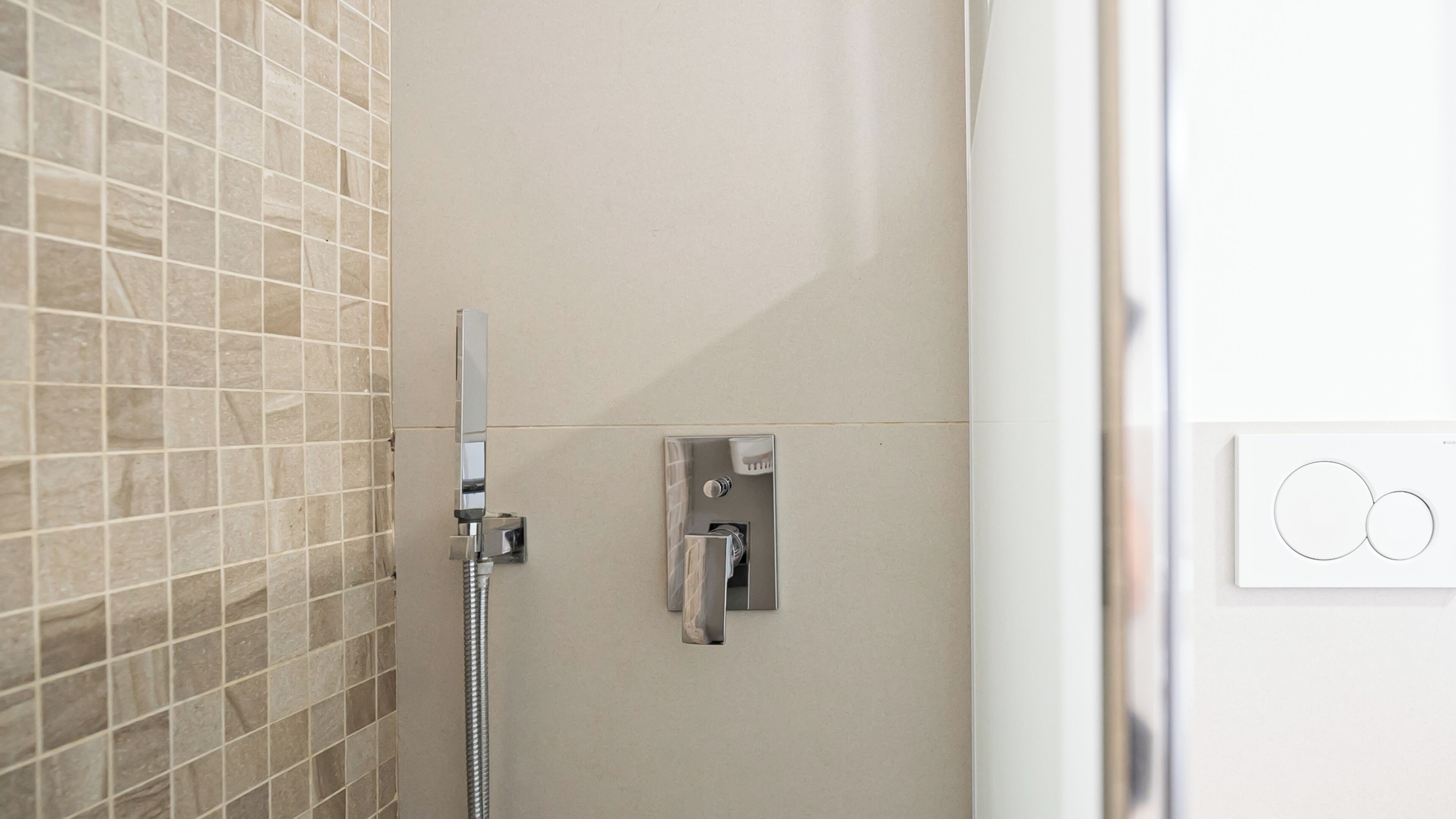 Ducha con cabezal de ducha de mano, panel de control en la pared y pared con azulejos.