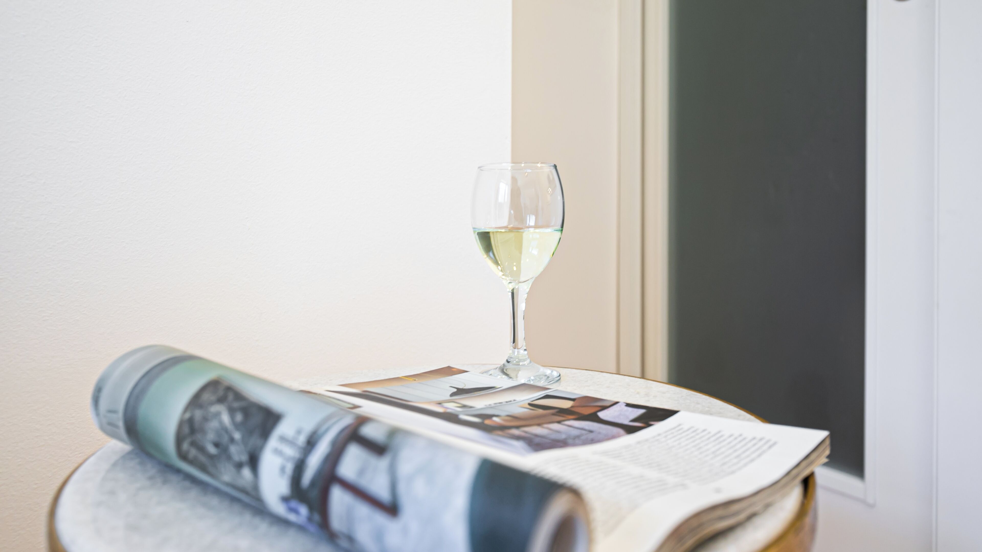 A glass of white wine on a table with a newspaper.