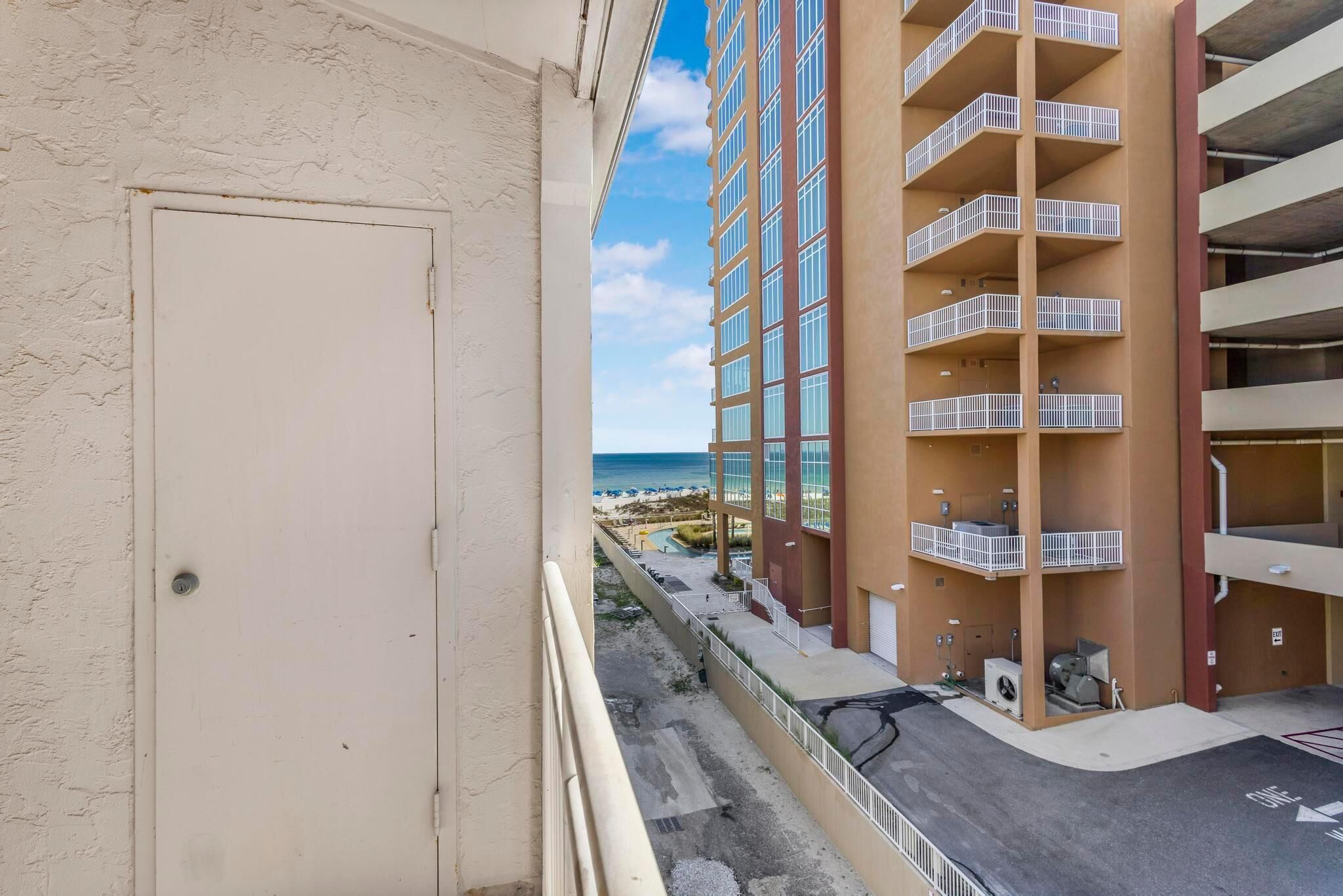 Un edificio de varios pisos con balcones, vista a la playa y zona de estacionamiento.