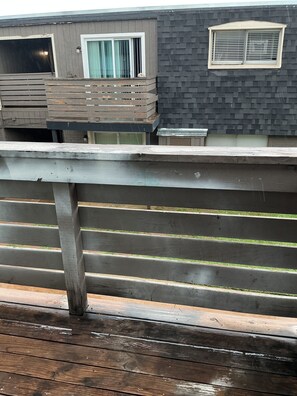 Eine Holzterrasse mit Geländer, ein Gebäude mit Fenster und Tür sowie eine Ziegelmauer.