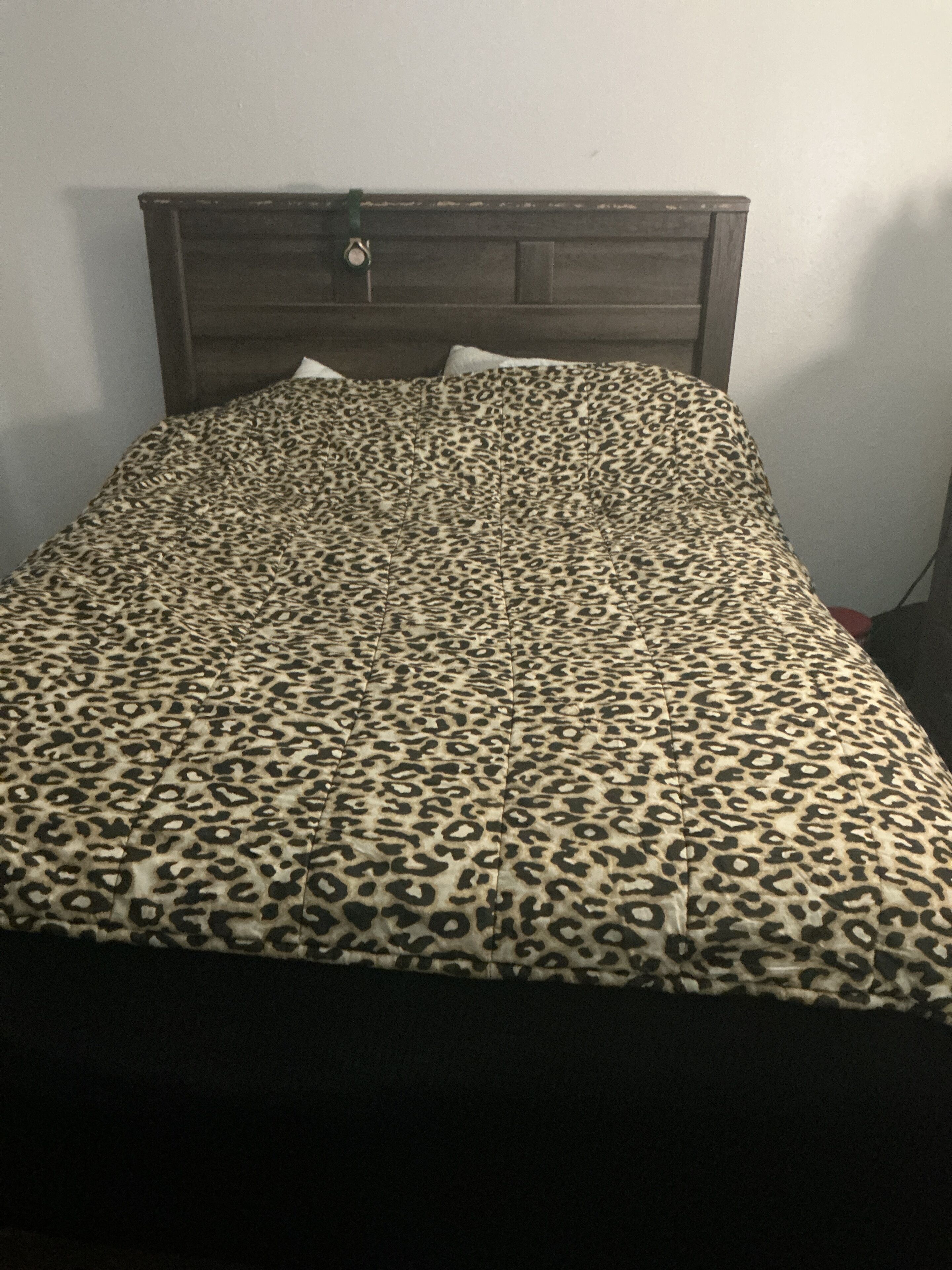 A bed with a leopard print bedspread, a wooden headboard, and a white pillow.