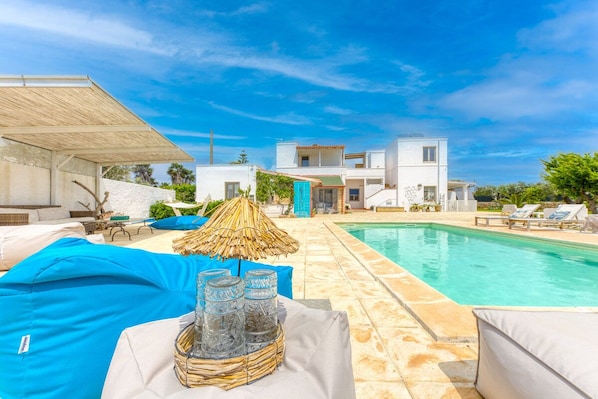 A poolside area with lounge chairs, a table with drinks, and a building in the background. - Sole Giallo - Salento Reservation (Capilungo)