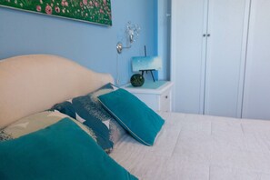 A bed with teal and white bedding, a small bedside table with a lamp, and a wall-mounted painting. - Suite Rilú con Idromassaggio -SalentoReservation (Capilungo)