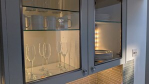 A kitchen with a built-in glass-front cabinet displaying wine glasses and dishes. - Luxury 3BR Home 20 Mins to London Garden Wi-fi (Gravesend)