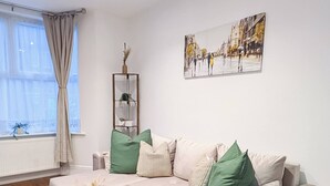 A living room with a sofa, a coffee table, a floor lamp, and a painting on the wall. - Luxury 3BR Home 20 Mins to London Garden Wi-fi (Gravesend)