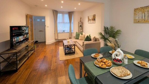 A living room with a sofa, coffee table, and a dining area with a table set for breakfast. - Luxury 3BR Home 20 Mins to London Garden Wi-fi (Gravesend)
